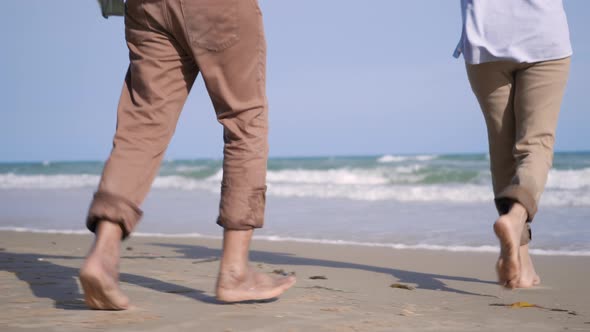 senior man and woman couple holding hands walking to the beach sunny with bright blue sky