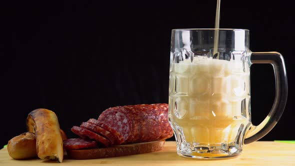 Pouring beer into the glass. Sausage with mug cold craft beer in a glass with water drops