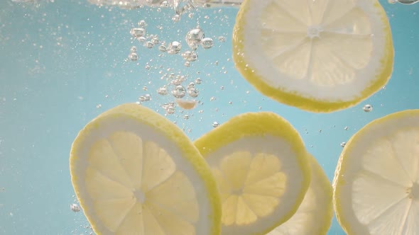 Slow Motion of Falling Lemon Slices Into Splashing Water on Blue Background