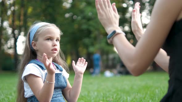 Pretty little child girl playing game with her mom with their hands outdoors in green summer park