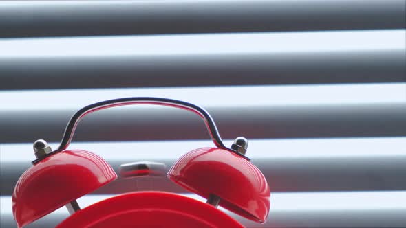 Red alarm clock in close up, ringing in early morning against the background closed blinds.