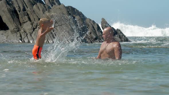 Cute Boy Splashes Water on Daddy Playing in Calm Sea Bay