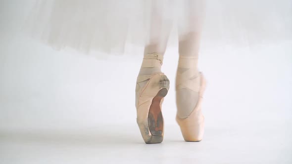 Female in a White Tutu Dance Ballet and Balancing in Pointe Shoes View of the Legs White Background