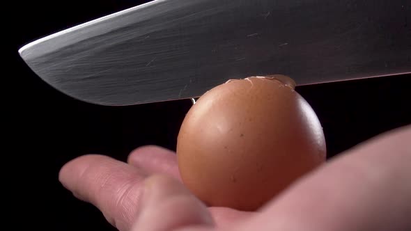 Chef breaks a raw egg with a knife on a black background 