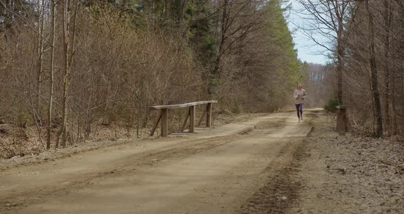 a girl in sportswear and sneakers runs along a forest road across a bridge in autumn