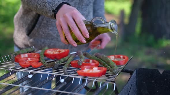 Making Grilled Vegetables  Pouring Olive Oil on Asparagus and Red Pepper on a Charcoal Grill
