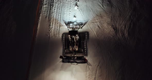 Aerial View. Orange Illuminated Snowcat Drives Up Along White Snowy Hill with Active Tourists on