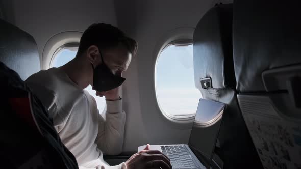 Businessman Flies in Airplane in Black Mask and Works on Computer