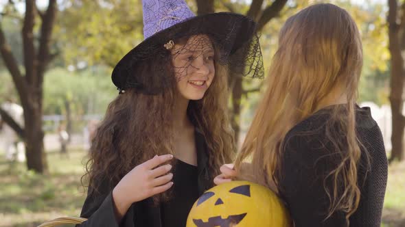 Cute Caucasian Redhead Girl Dressed in Witch Costume Talking To Her Blonde Friend. Two Little