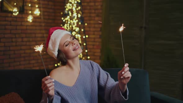 Smiling Girl Relaxing and Playing with New Year Sparklers in Cozy Room