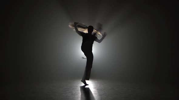 Woman with Long Hair Practicing Capoeira in Darkness Against Spotlight in Studio