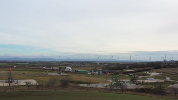 [DRONE]revealing shot of a scenery with multiple oil derricksing and wind turbines in the background