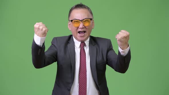 Mature Japanese Businessman Wearing Sunglasses Against Green Background