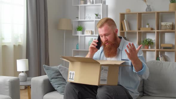 Redhead Man Sitting on Sofa with Opened Parcel Express Complaints to Seller or Courier on the Phone