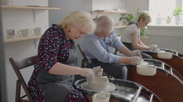 Three Elderly People Work on a Potter's Wheel in Slow Motion