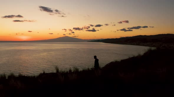 Silhouette of a boy is passing on a rock near the ocean at sunset 