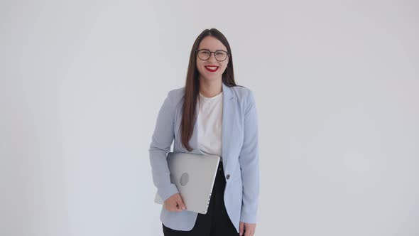 A Beautiful Young Business Woman is Standing with a Laptop Under Her Arm and Fooling Around in Front