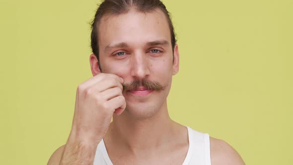 Portrait of Funny Caucasian Man Smiling Over Yellow Background Making Face While Twirling Mustaches