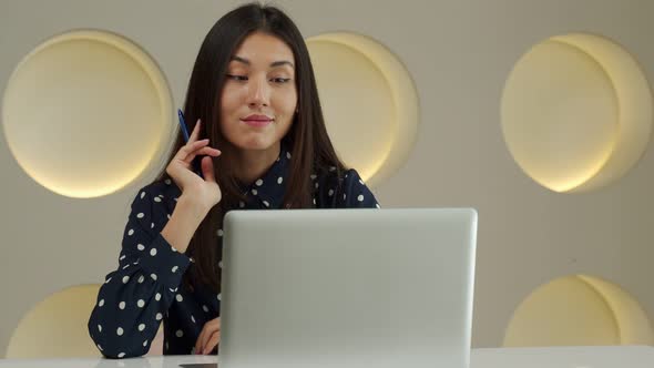 Thoughtful Business Asian Woman Working at a Computer Smiling and Looking Into the Distance Thinking