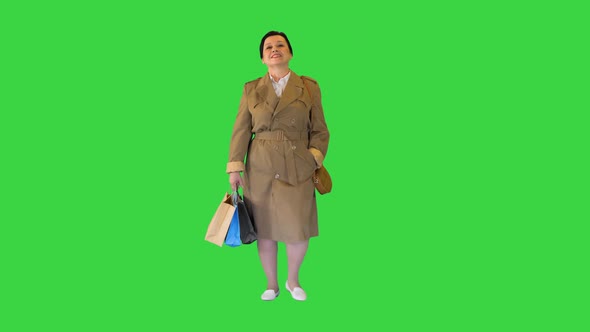 Mature Brunette Woman in a Coat with Shopping Bags Walking on a Green Screen, Chroma Key.