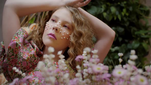 Portrait of Adorable Young Girl with Artistic Makeup Posing Near Flowers