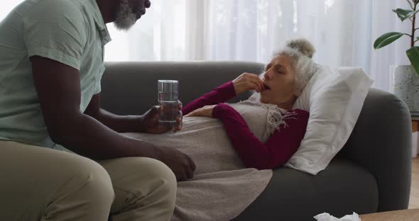 African american man giving medication to his sick wife in the living room at home