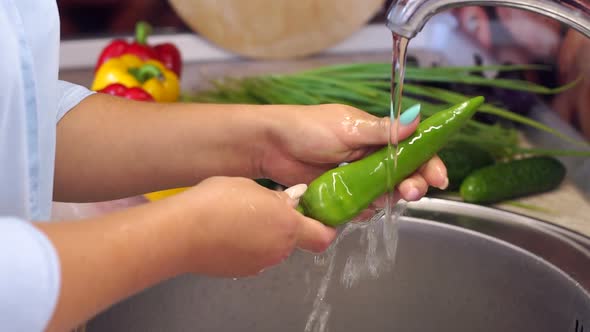 Closeup of Young Girl Washing Chili Peppers in the Sink at Home in the Kitchen