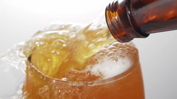 Beer is pouring with bubbles and foam in large beer glass from bottle on white background close up.