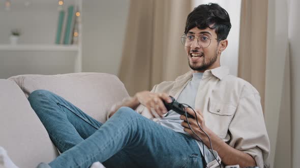 Arab Guy Bearded Man with Glasses Lying on Couch at Home Playing Console Online Video Game
