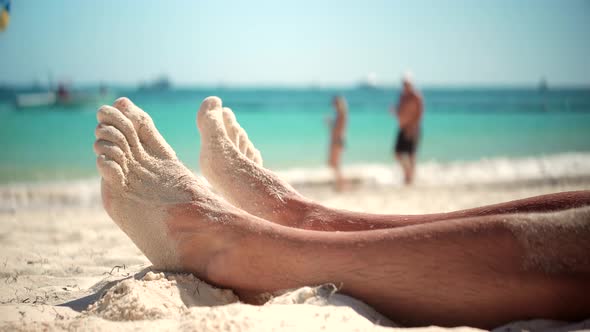 Man Lying On Beach And Moving Legs On Holiday Vacation. Man Legs On Beach Sun Lounger Sandy Shore.