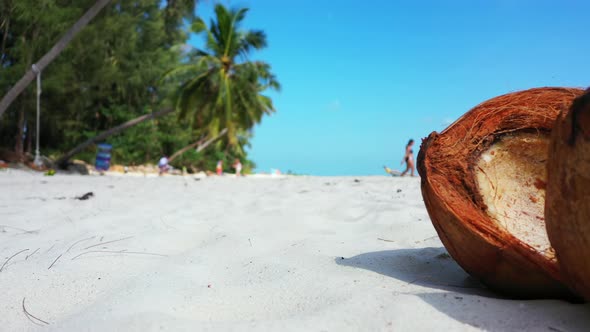 Cracked coconut lying on white sand beach on tropical island. Young girl going into the sea in the b