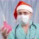 A Cheerful Doctor in a Santa Claus Hat Plays with an Enema and Gestures Approves of the Procedure - VideoHive Item for Sale