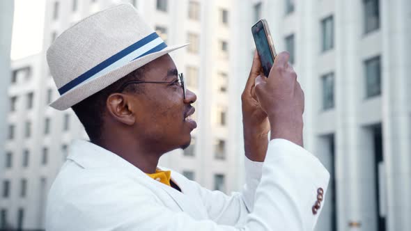 Black man tourist in white suit and glasses holds smartphone