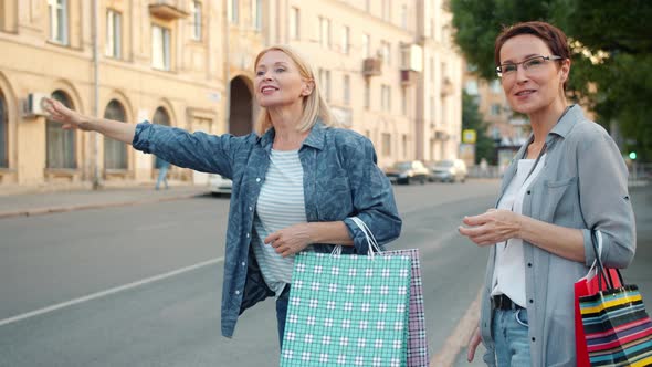 Smiling Women with Shopping Bags Hailing Taxi Waving Hand Outdoor in City Street