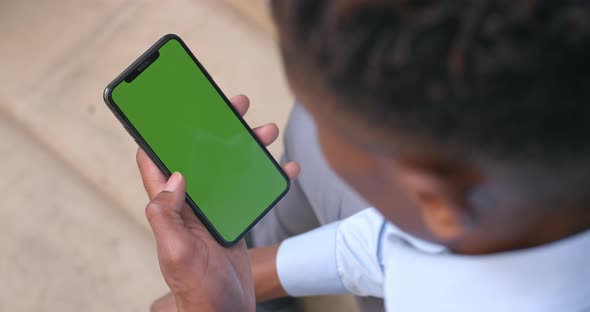 Over Shoulder View of Afro American Businessman Sitting and Holding Smartphone with Green Screen in