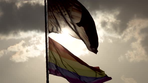 Rainbow LGBT gay pride flag waving in the wind 4 and the American flag waving with sun backlit under