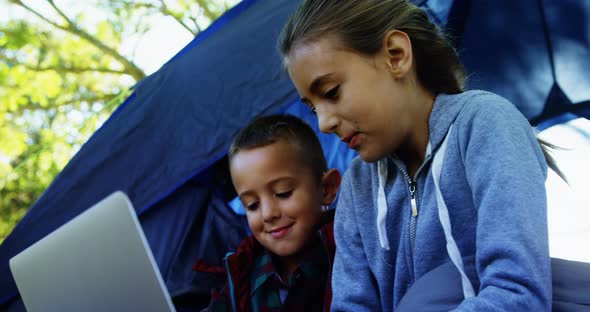 Siblings using laptop outside the tent at campsite
