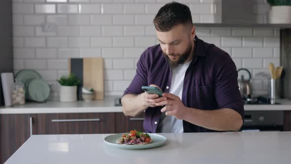 Young Man Photographing Food with Smartphone in Kitchen, Copy Space