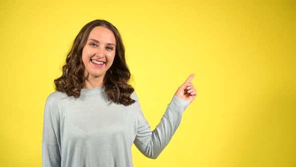 Attractive Curly Young Woman Points Finger Away Isolated on Yellow