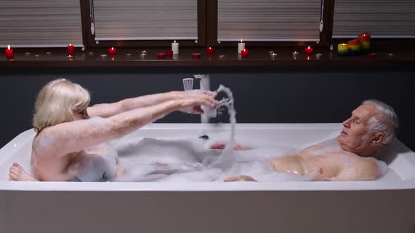 Senior Couple Grandfather and Grandmother Is Taking Bath, Splashing Water in Bathroom with Candles
