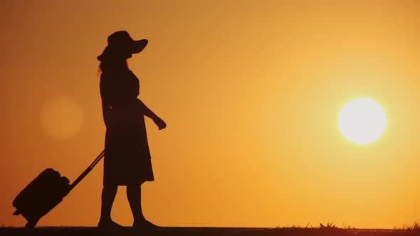 Silhouette girl traveler with suitcase walking on country road 