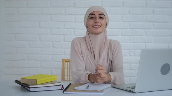 A Young Muslim Woman in a Hijab Sits at a Table and Smiles Happy Because She Can Get an Education