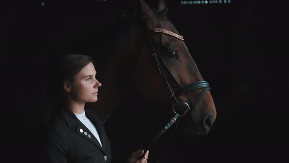 Girl Standing With Her Dark Brown Horse In The Stable Holding Its Lead Rope