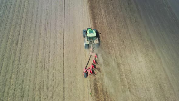 A green tractor with a red plow plows the soil.