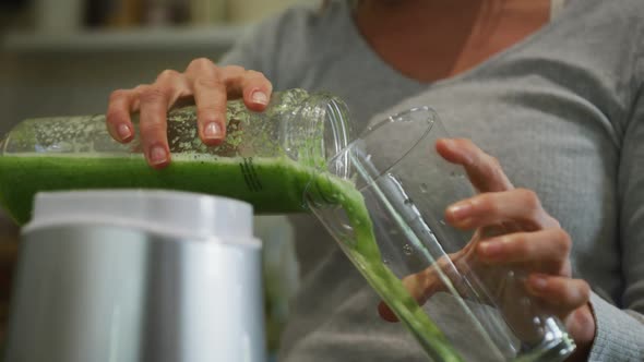 Caucasian woman pouring green vegetable smoothie into glass container in kitchen