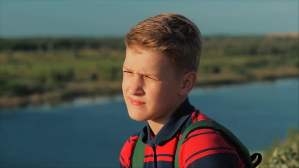 Teenager in a Red Shirt with a Backpack on His Back, at Sunset, Sitting on a High Hill and Looking