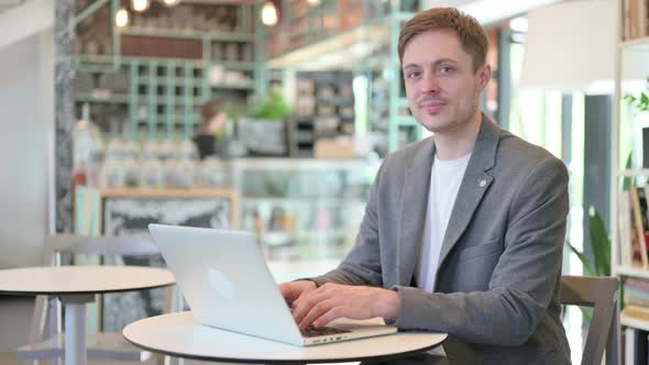 Young Man with Laptop Smiling at Camera