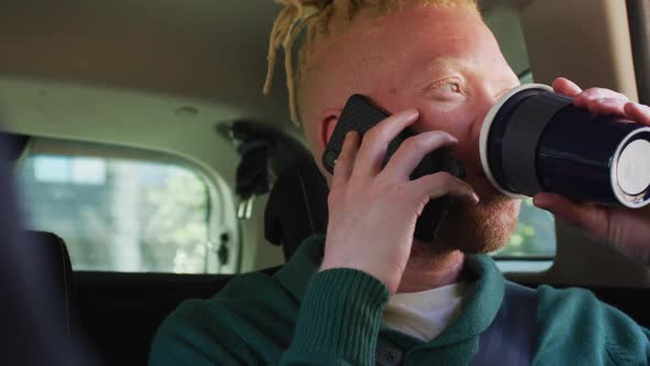 Happy albino african american man with dreadlocks sitting in car talking on smartphone