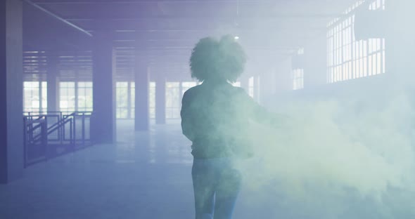 Mixed race woman holding green flare walking through empty building