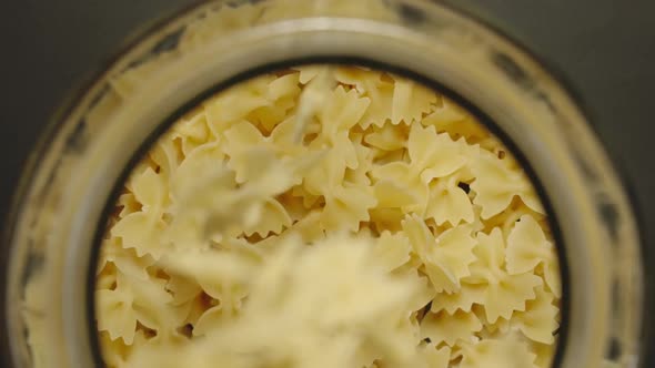 Uncooked Bow Tie Pasta Fall Into Glass Jar On Black Background 